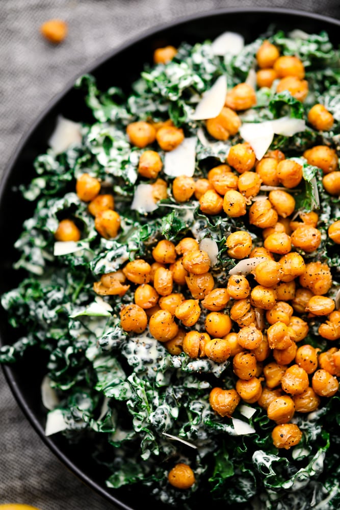 close up of kale caesar salad in a black bowl topped with chickpea croutons