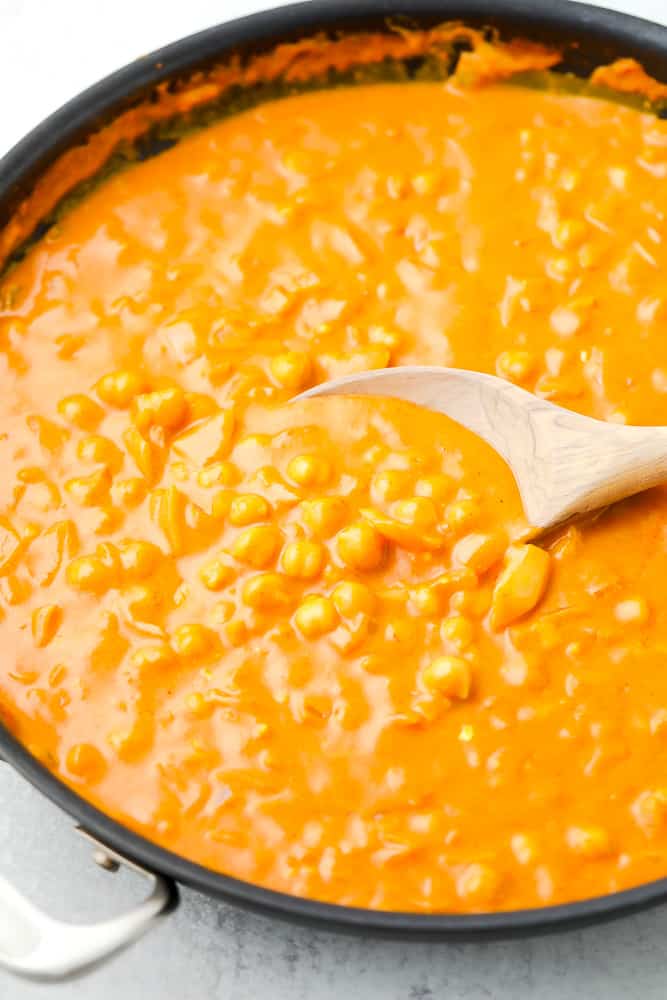 wooden spoon stirring an orange sauce with chickpeas in a large skillet