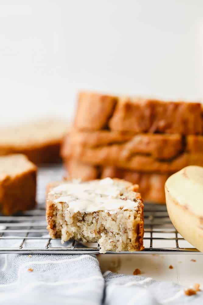 buttered and bitten slice of banana bread on a cooling rack