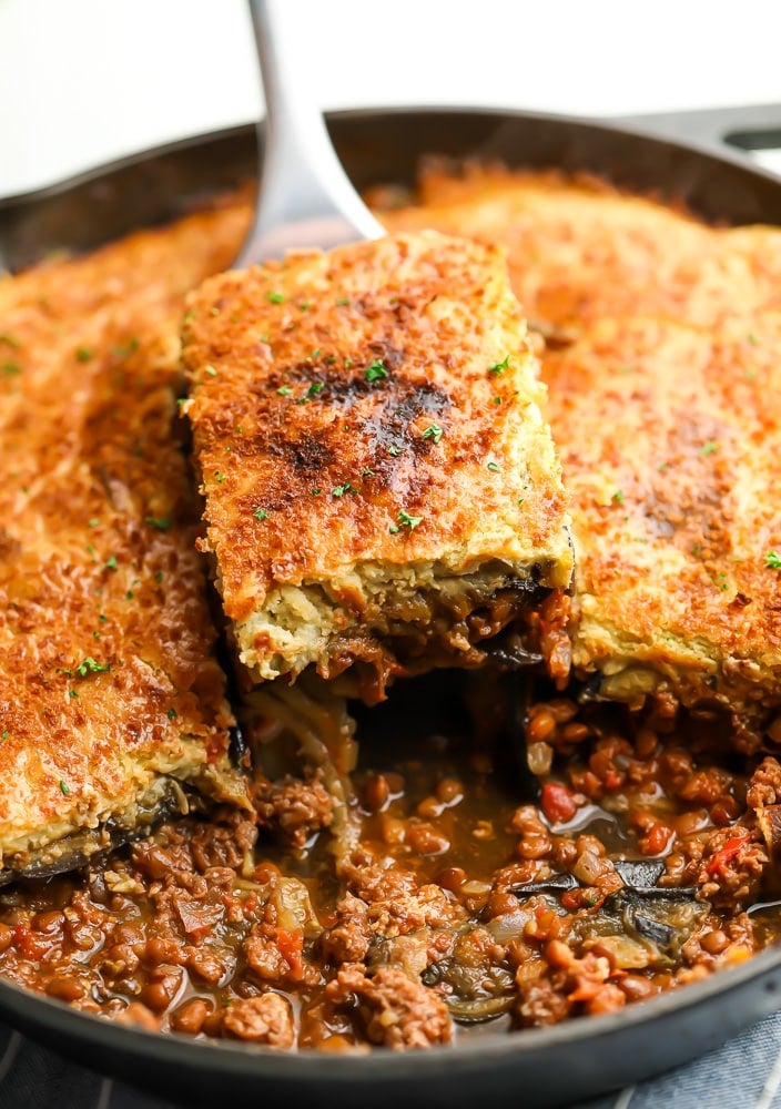 Spoon taking a slice of golden brown moussaka out of a baking dish