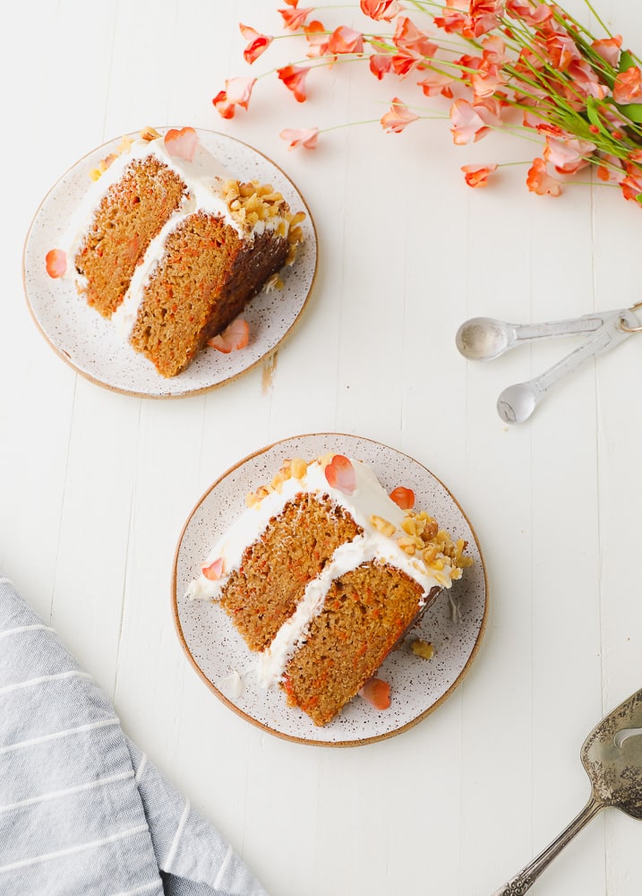 looking down on a few pieces of cake on plates with white frosting, orange cake and flowers