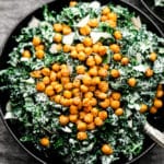 close up of green caesar salad in a black bowl with chickpea croutons