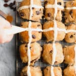 square photo of buns with icing going on them in cross shapes