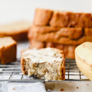 buttered and bitten slice of banana bread on a cooling rack