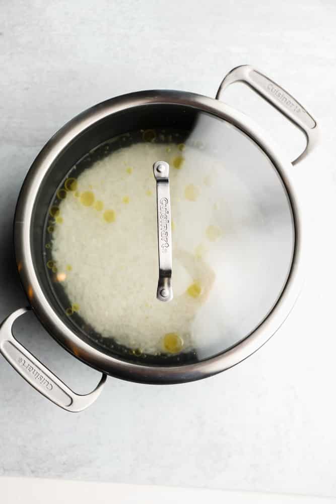 white rice, oil, and water in a black pot with a glass lid on top