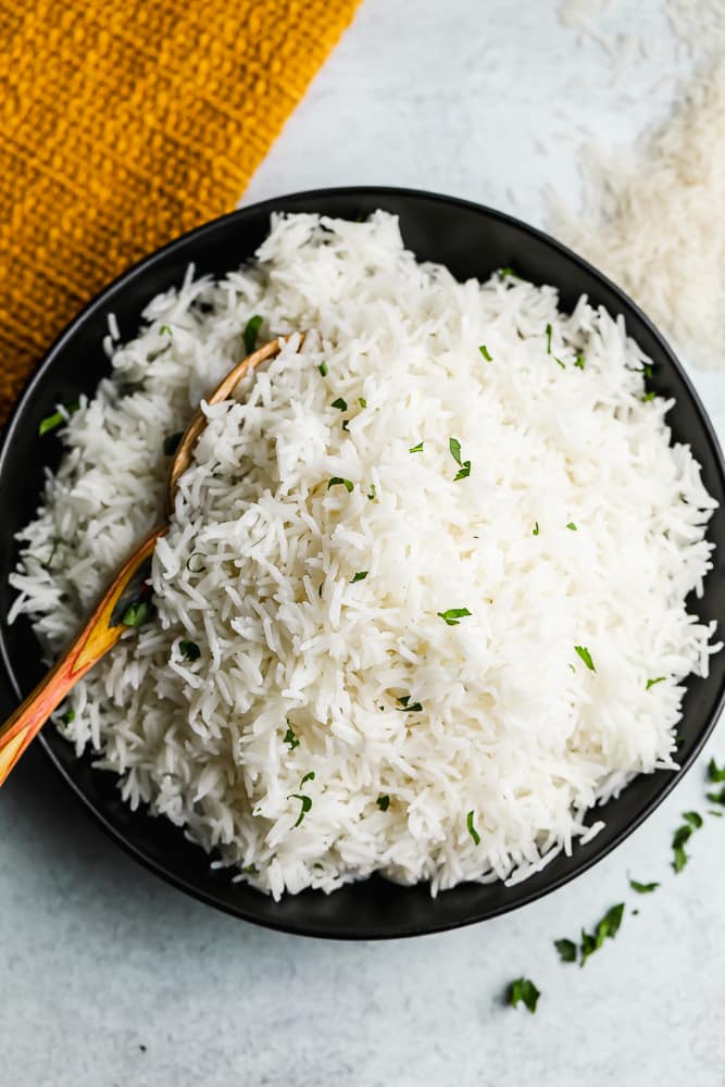 black bowl filled with cooked white rice and a wooden spoon