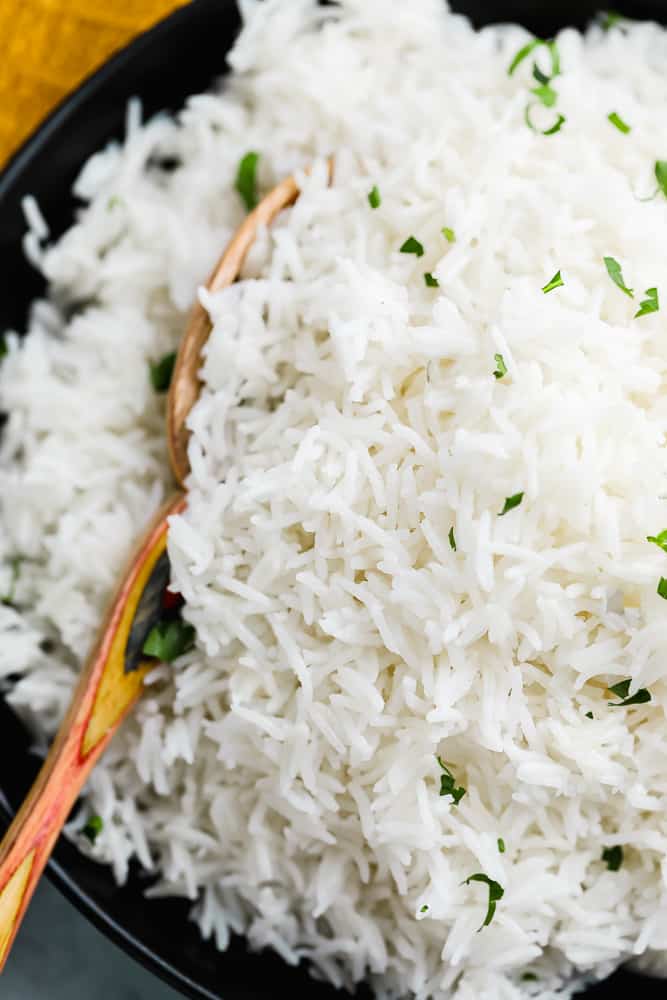 close up on a wooden spoon taking a scoop of white rice out of a black bowl