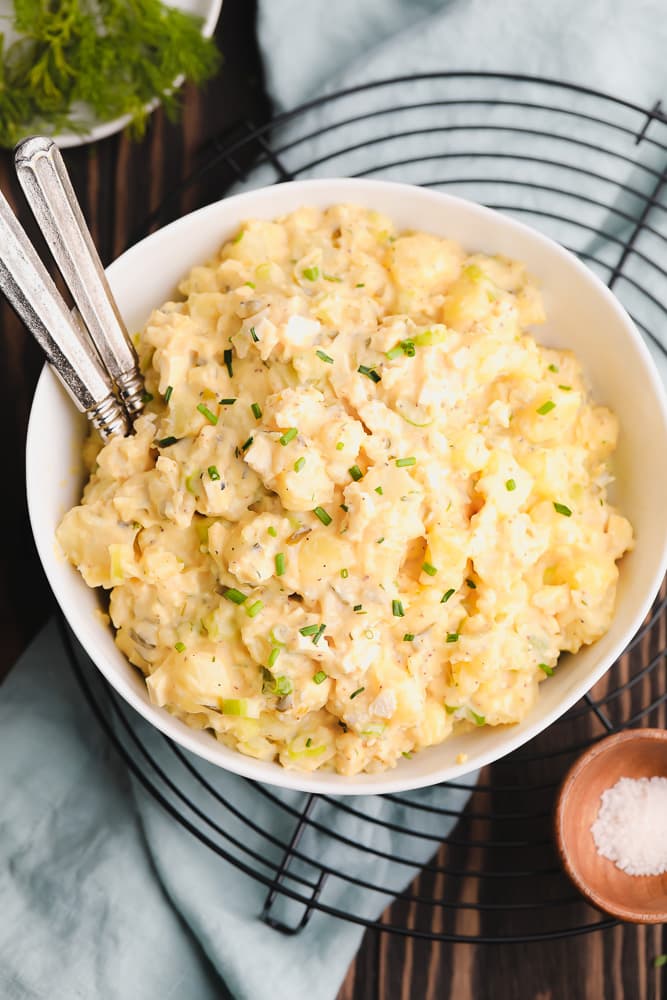 bowl of potato salad with two forks in it, on black round cooling rack.