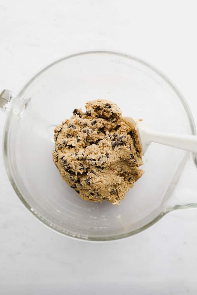 stirring raw cookie dough with a white spatula in a glass bowl