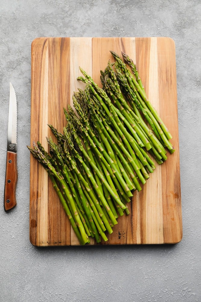 raw asparagus on a wood board next to a knife