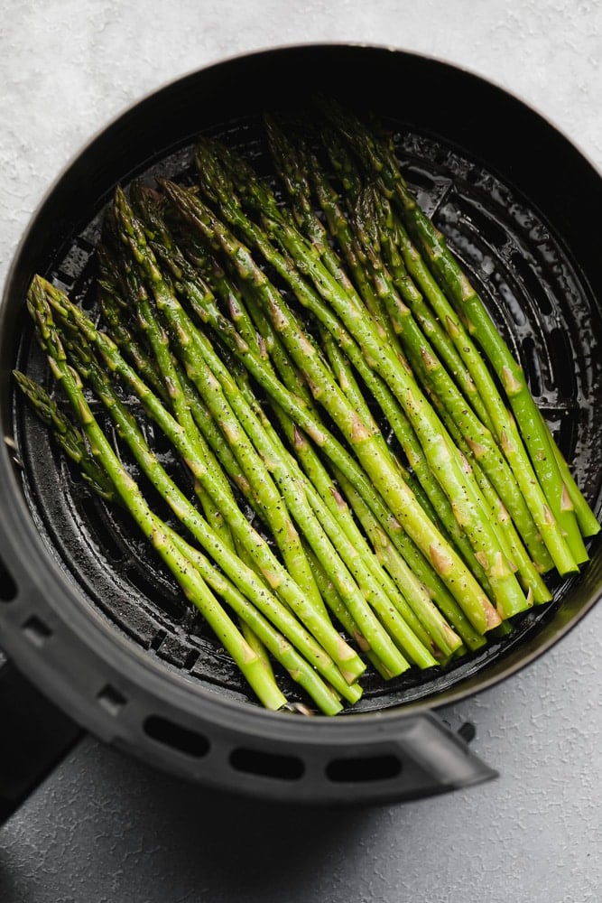 seasoned raw asparagus in an air fryer basket