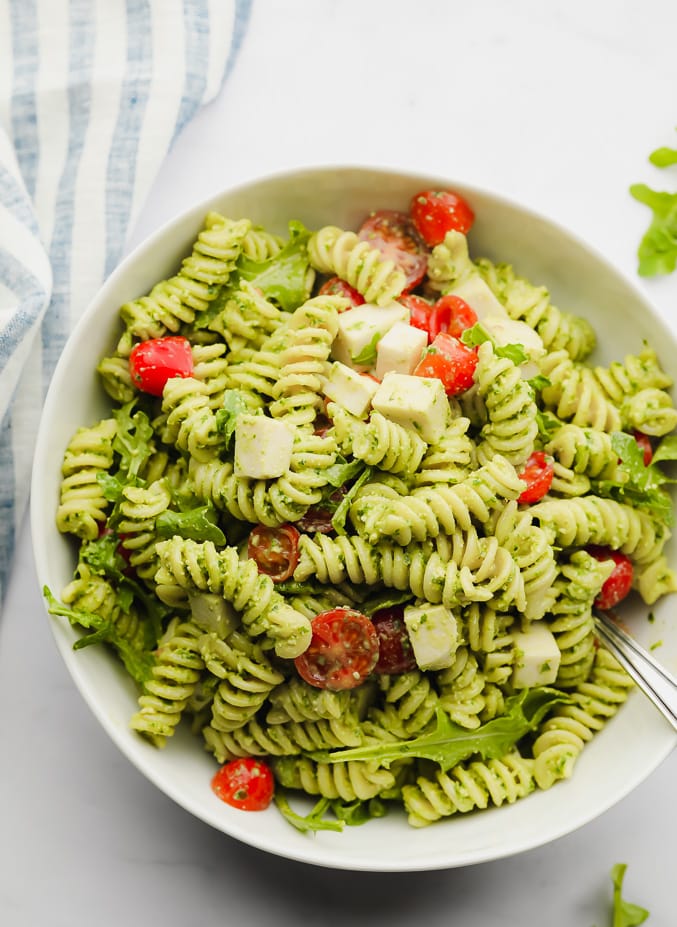 green pasta salad with tomatoes in a white bowl