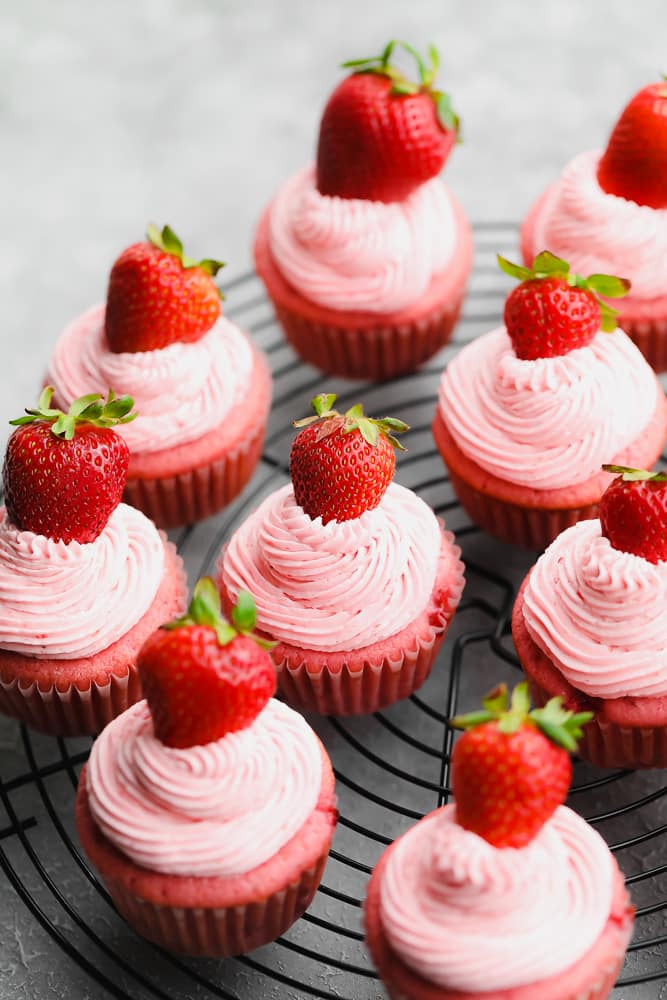 close up of many vegan strawberry cupcakes on a black rack