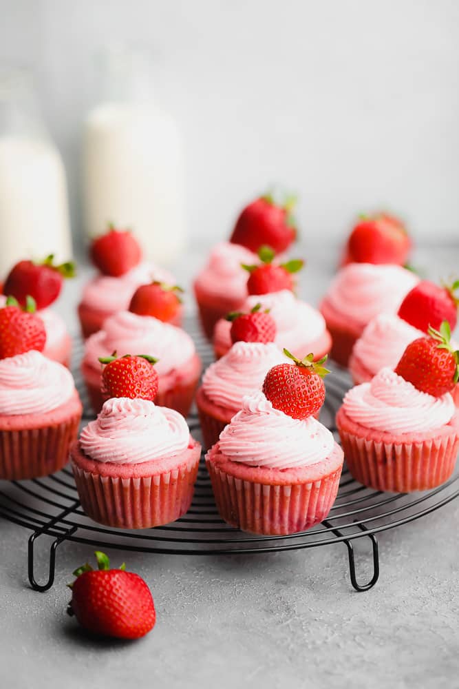 many red cupcakes with pink frosting on a round cooling rack