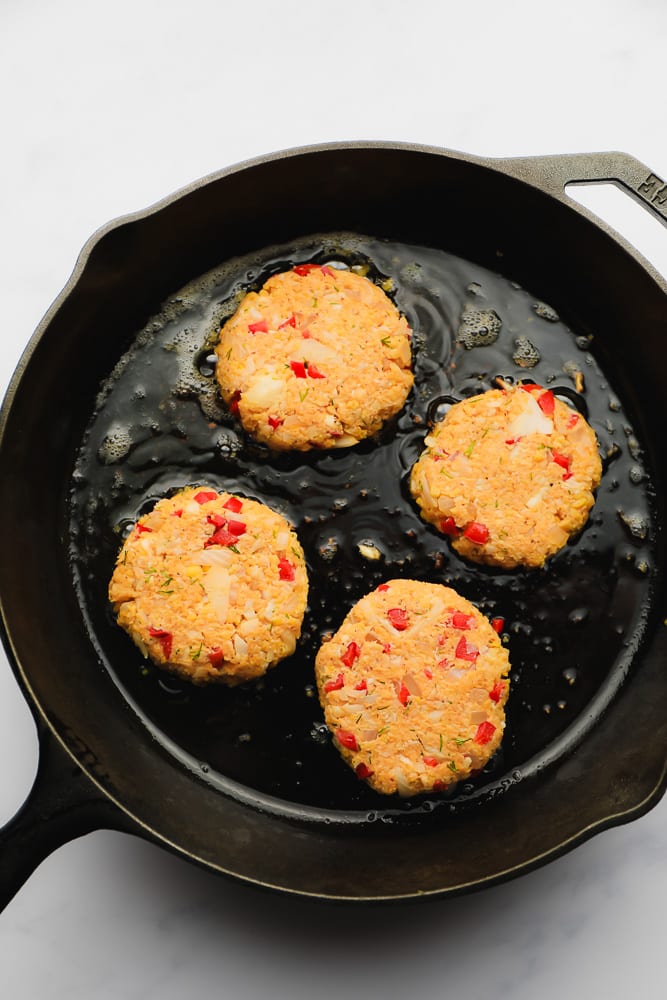 vegan crab cakes frying in a cast iron skillet