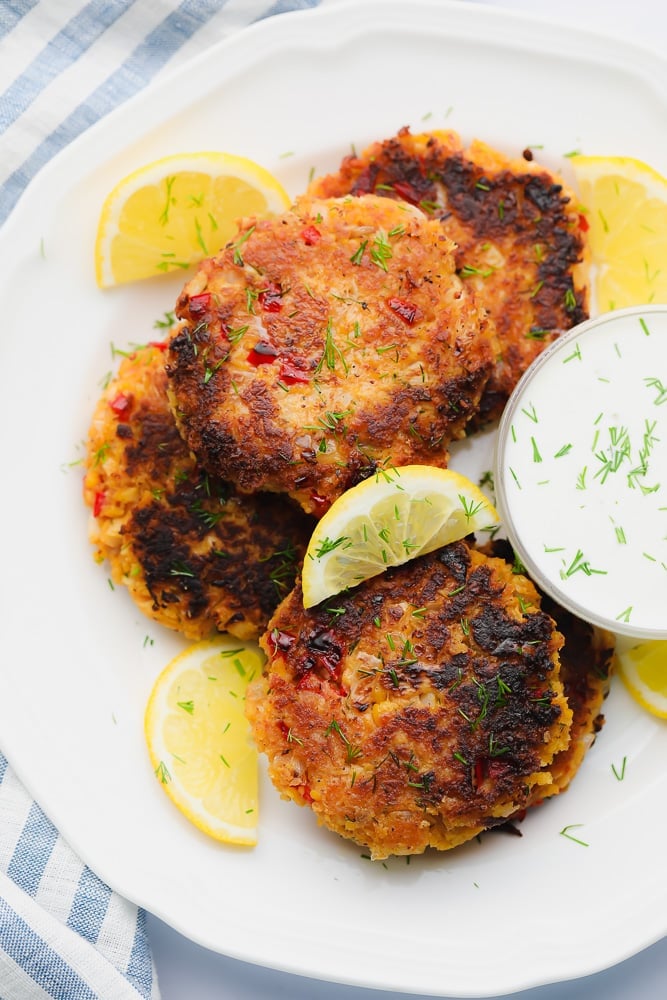 white plate with fried vegan crab cakes next to white dipping sauce and lemon wedges