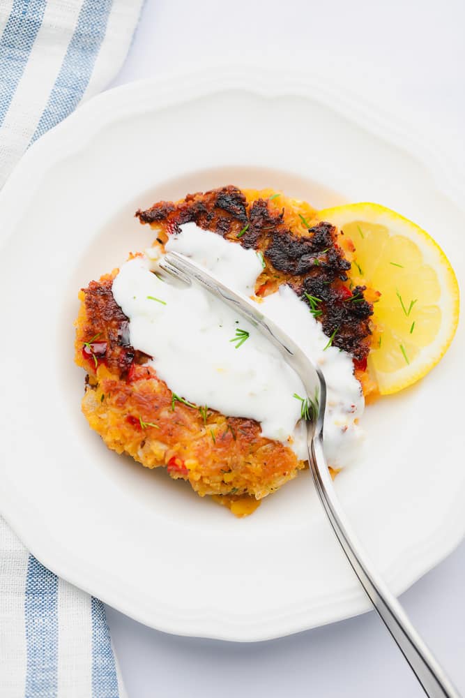 fork cutting into a sauce-covered vegan crab cake on a white plate