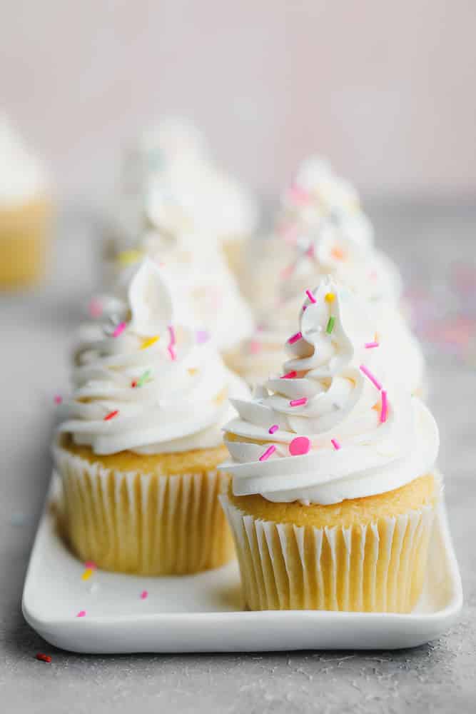 several cupcakes on a white tray with sprinkles and white frosting