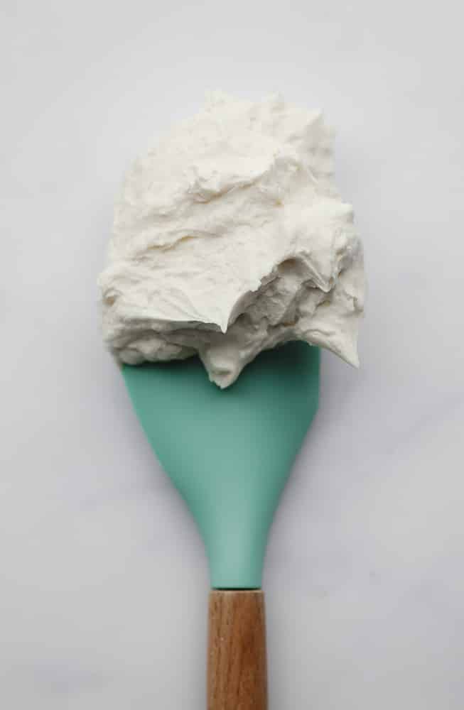 spatula with frosting on it, teal colored and white backdrop