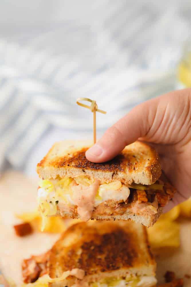 woman's hand lifting 1 half of a vegan reuben sandwich