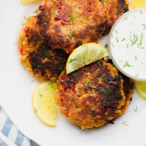 white plate with fried vegan crab cakes next to white dipping sauce and lemon wedges