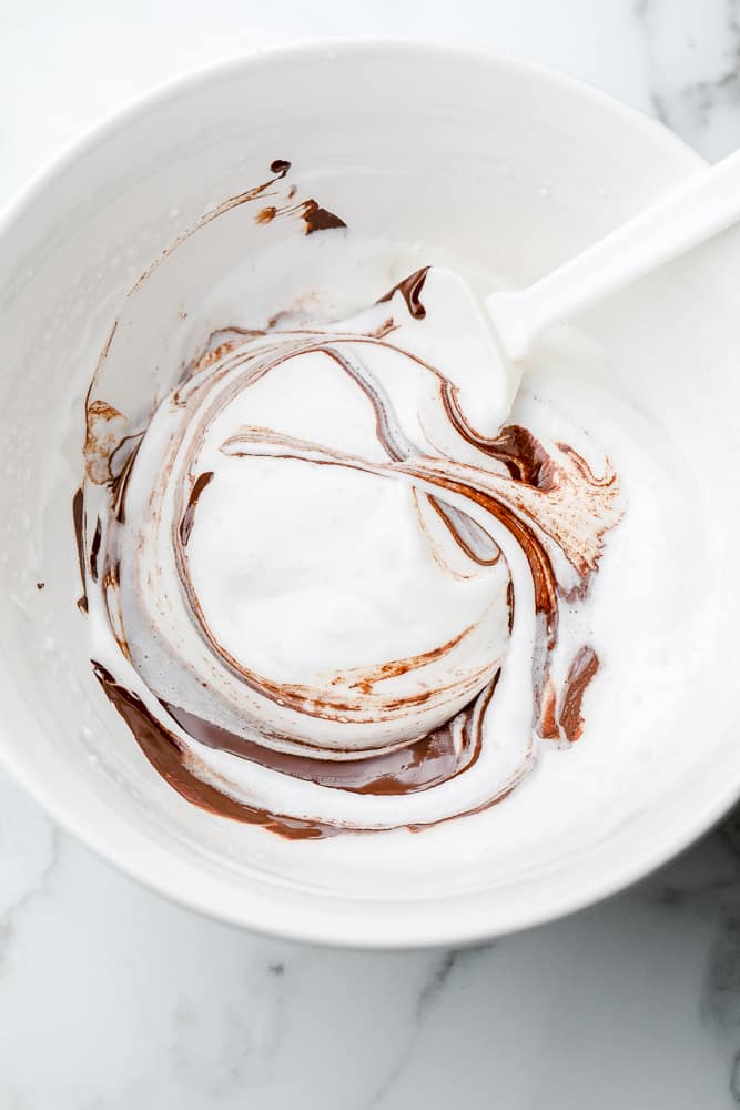 white spatula folding white cream and melted chocolate together in a white bowl