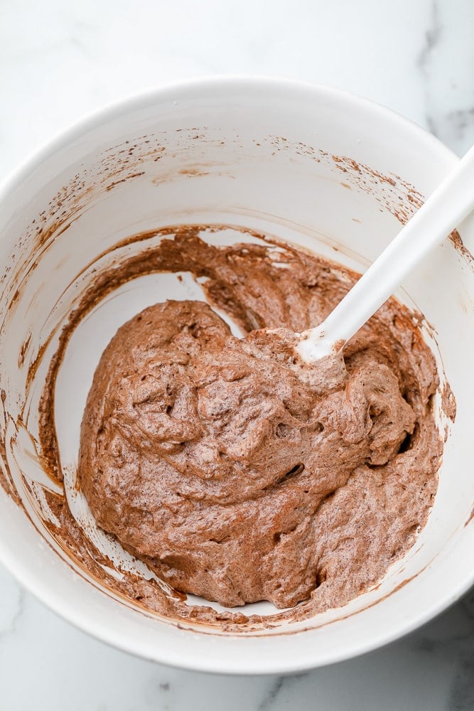 white spatula mixing chocolate mousse in a white bowl