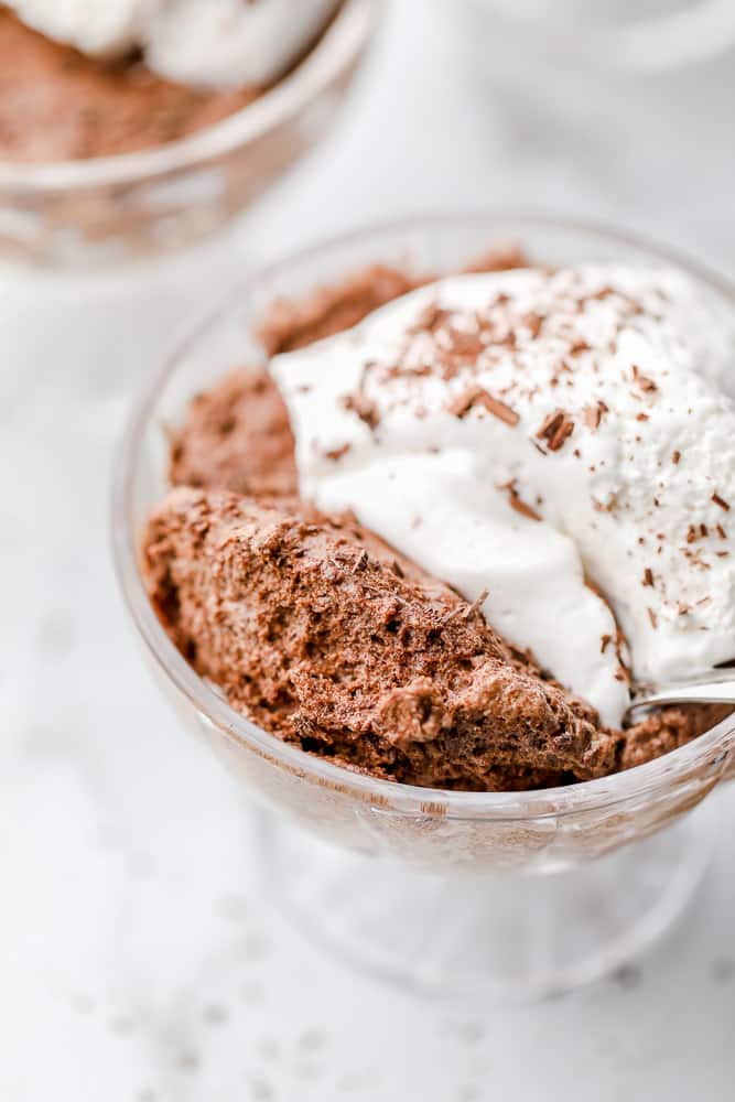 close up on a glass dessert cup holding chocolate mousse topped with whipped cream