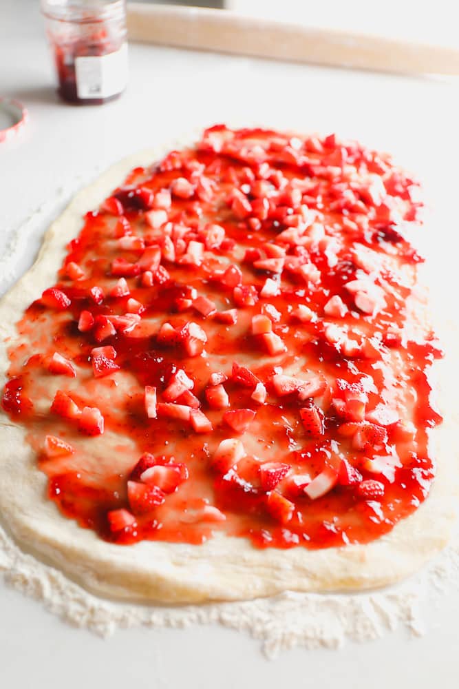 cinnamon roll dough on counter spread out with berries and jam on it