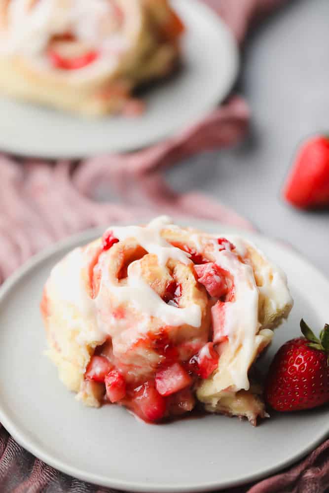 one roll on a grey plate with icing and strawberries