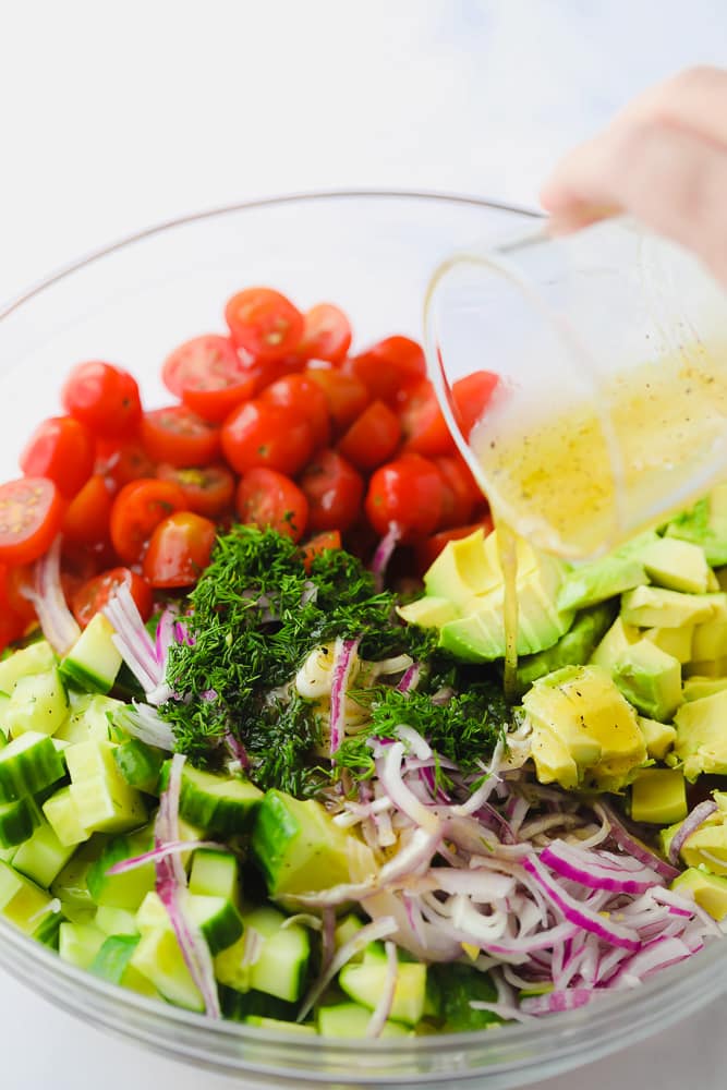 pouring lemon dressing over a bowl of chopped vegetables