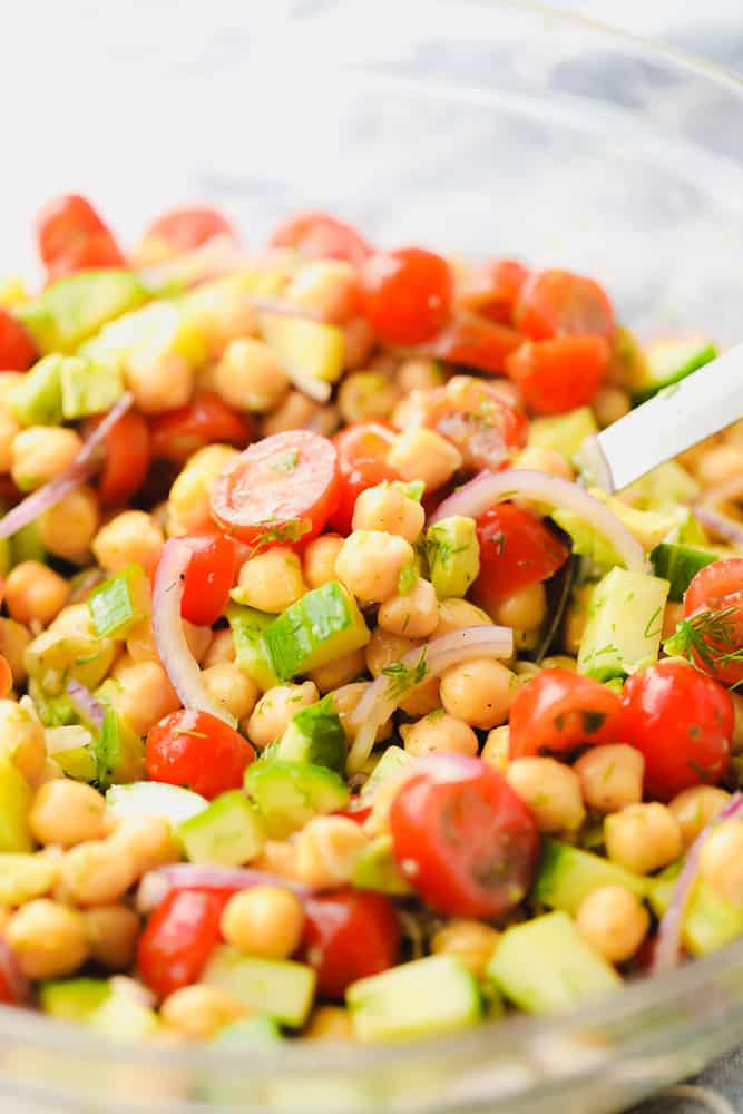 close up on a chickpea salad in a glass bowl with tomatoes, cucumber, and onion