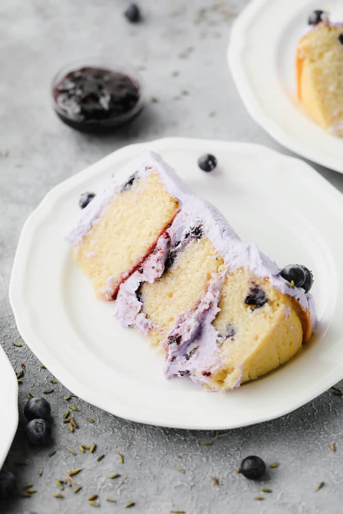 purple frosted cake with blueberries on a white plate, triple layer
