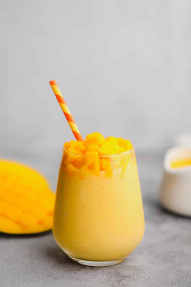 yellow smoothie in a glass garnished with mango chunks and a yellow and red straw