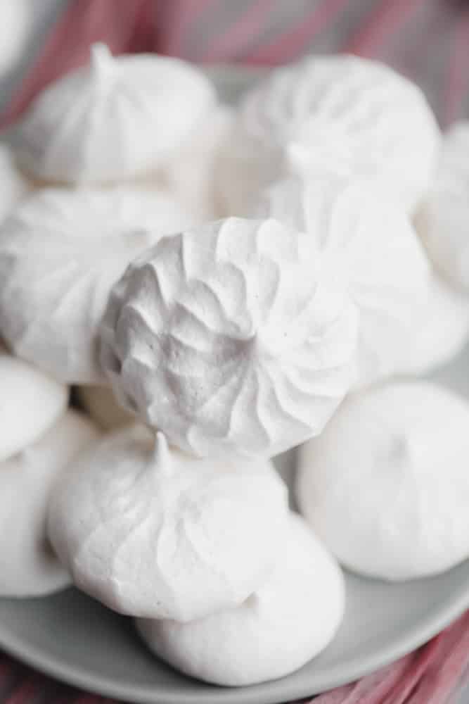 close up on a pile of white vegan meringues cookies on a small grey plate