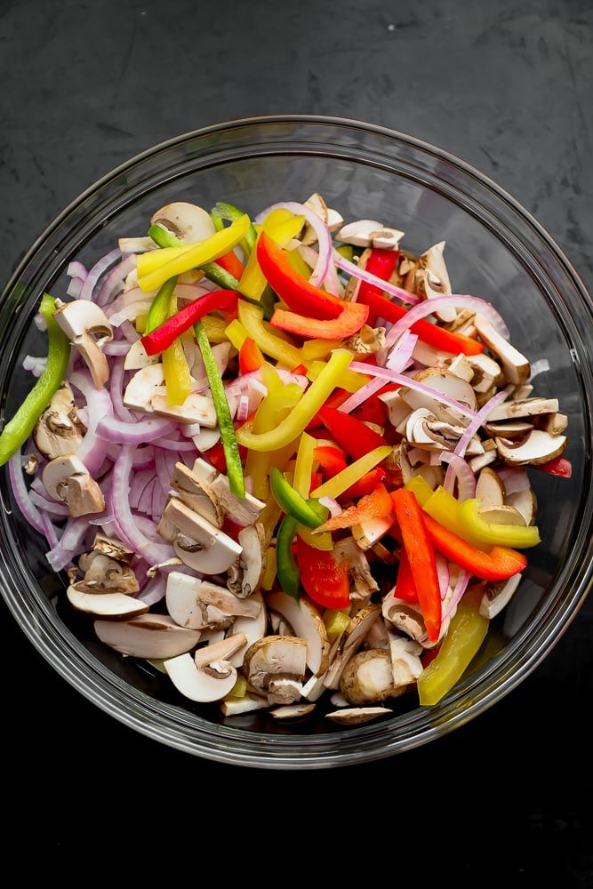 large glass bowls with sliced bell peppers, red onion, and mushrooms inside for vegetarian fajitas