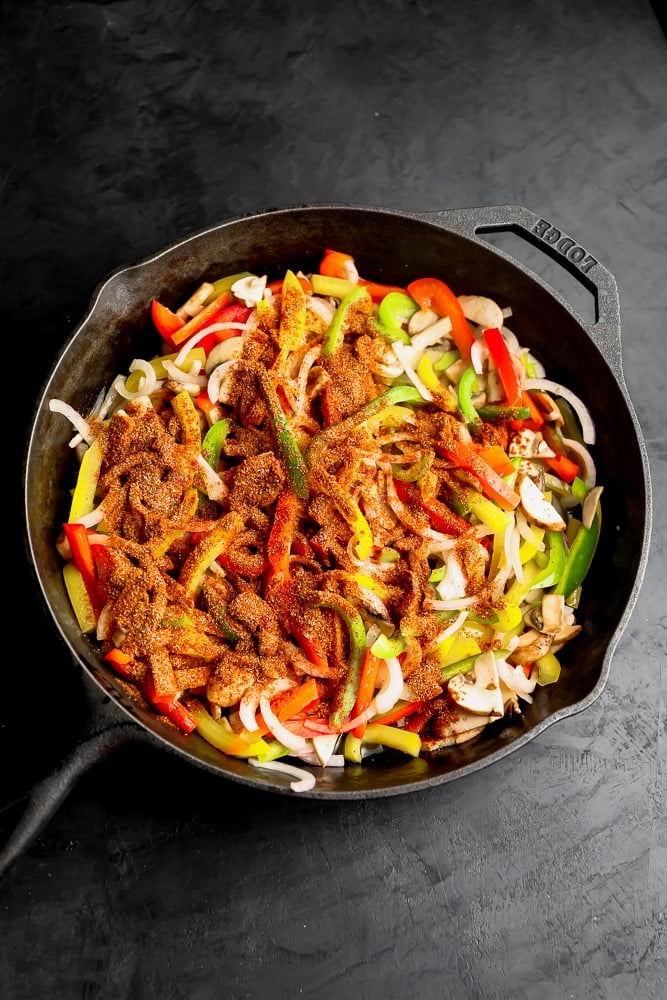 raw sliced veggies with seasonings on top in a black skillet