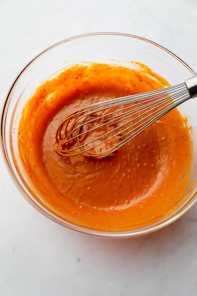 a metal whisk in a glass bowl with orange sauce