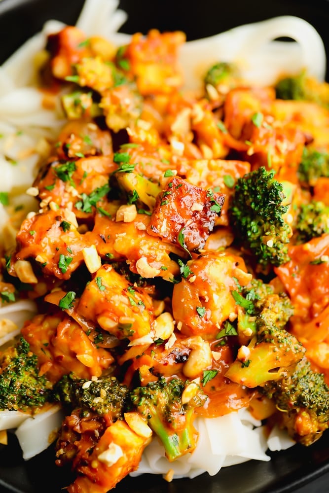 close up on a tempeh and broccoli stir fry on top of white noodles in a black bowl