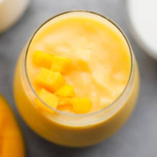 square image of an orange smoothie with mangos on top