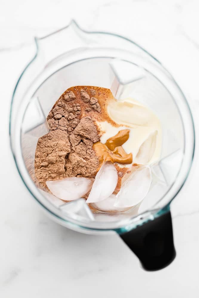 overhead view of chocolate powder, ice, and milk in a blender