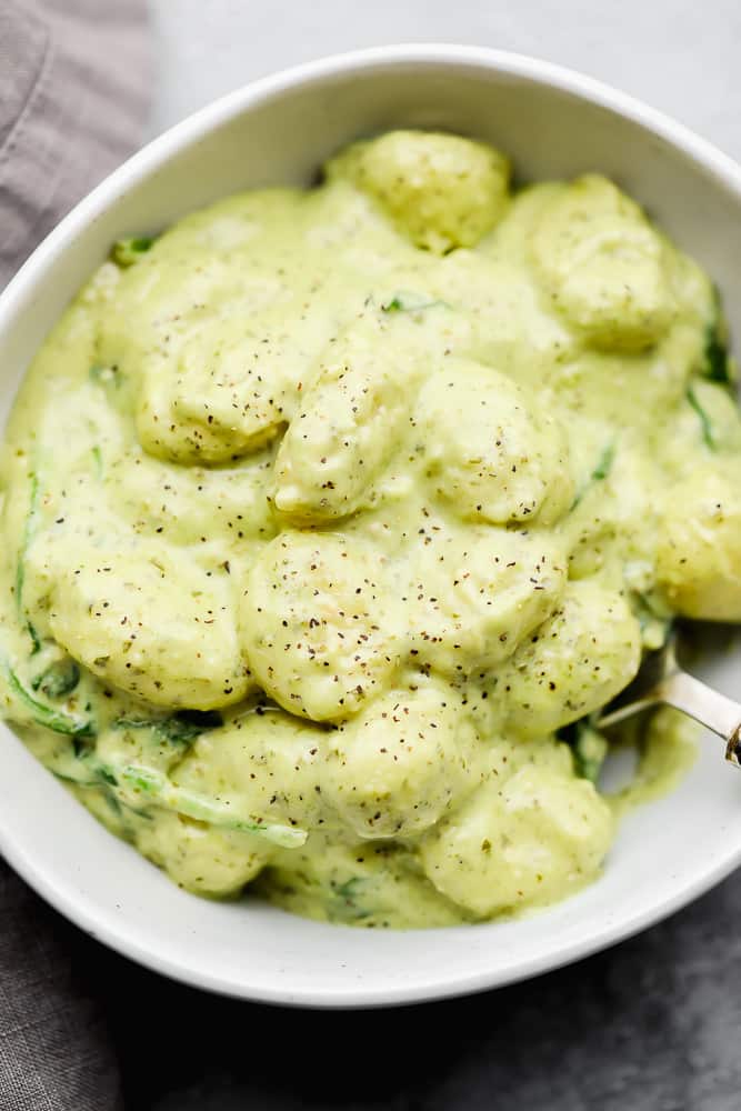 white bowl filled with gnocchi and a green creamy sauce