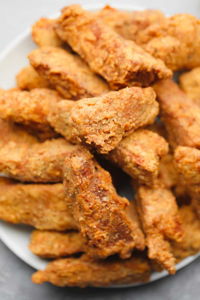 close up on a large plate filled with golden brown fried vegan chicken pieces