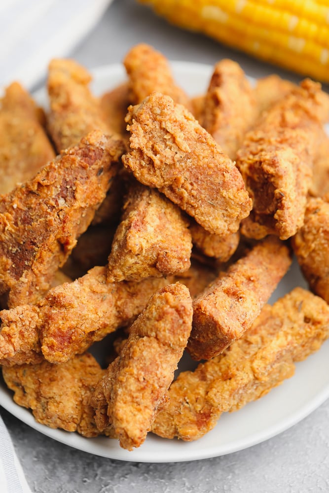 close up on a large plate filled with golden brown fried vegan chicken pieces