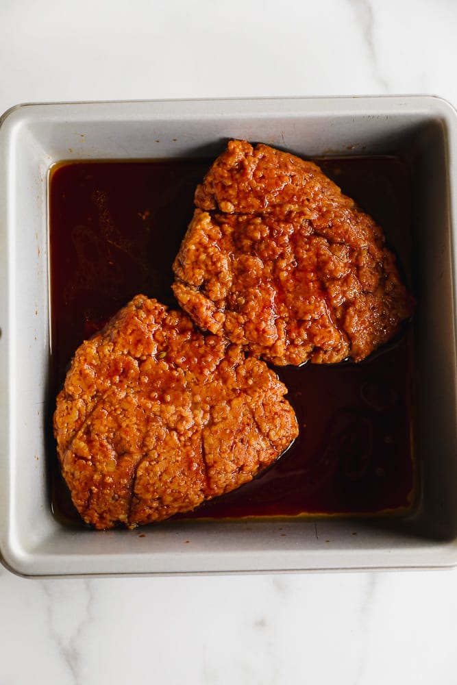 2 orange seitan patties marinating in a dark brown liquid