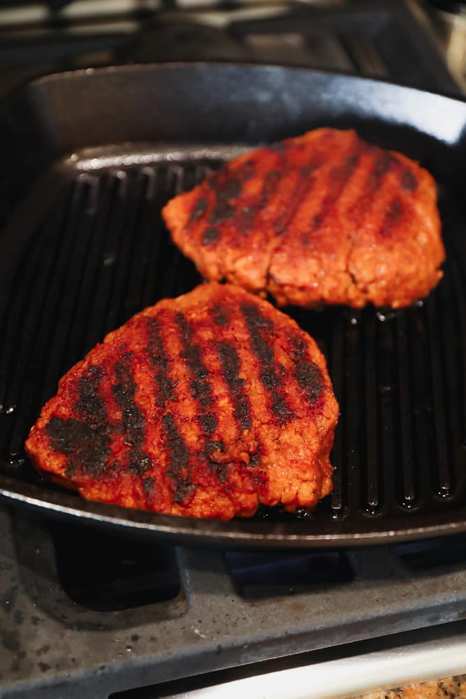 grilling 2 orange seitan patties in a black grill pan