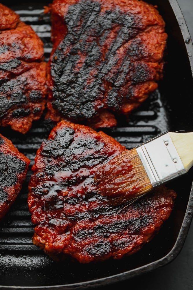 brushing red sauce on a charred vegan steak in a grill pan