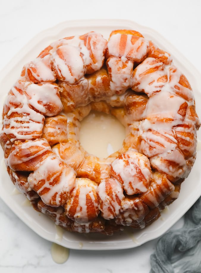 baked golden brown monkey bread on a white plate, covered in white icing