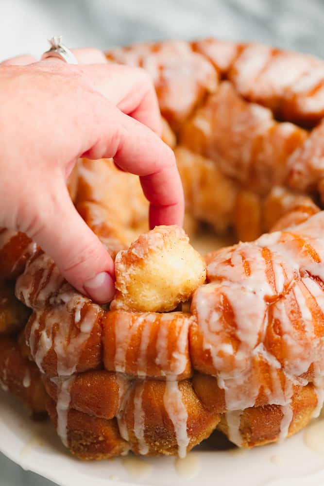 womans hand taking a ball of dough from loaf of baked golden brown monkey bread