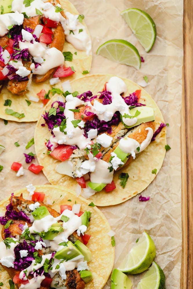 corn tortillas topped with vegan fish, purple cabbage, and a white sauce on parchment paper